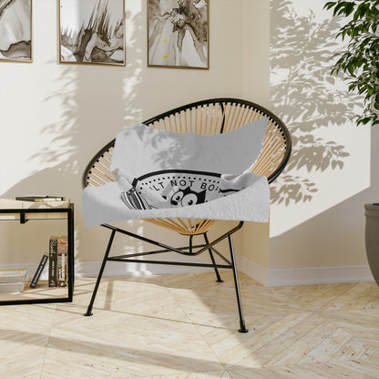 The blanket draped over a round rattan chair in a bright living room with framed prints on the wall behind it.