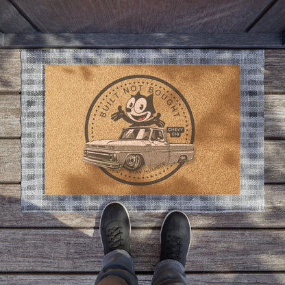 The doormat on a wooden porch with a person standing on it in black shoes.