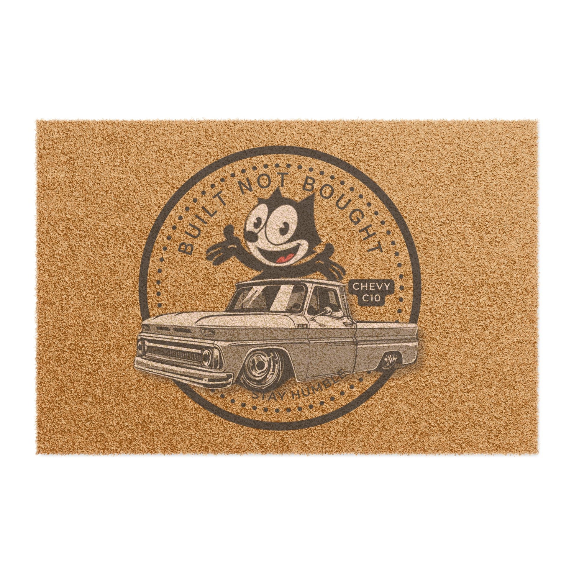 Coir doormat printed with a round Built Not Bought badge: a cartoon cat leaning on a lowered classic pickup truck, with Stay Humble along the bottom.