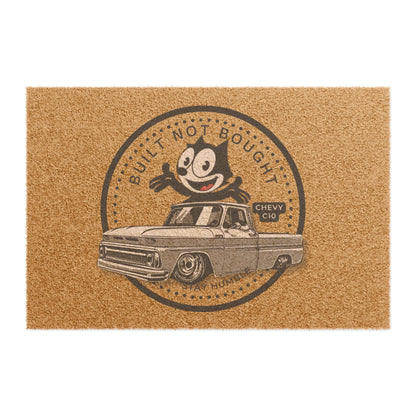 Coir doormat printed with a round Built Not Bought badge: a cartoon cat leaning on a lowered classic pickup truck, with Stay Humble along the bottom.