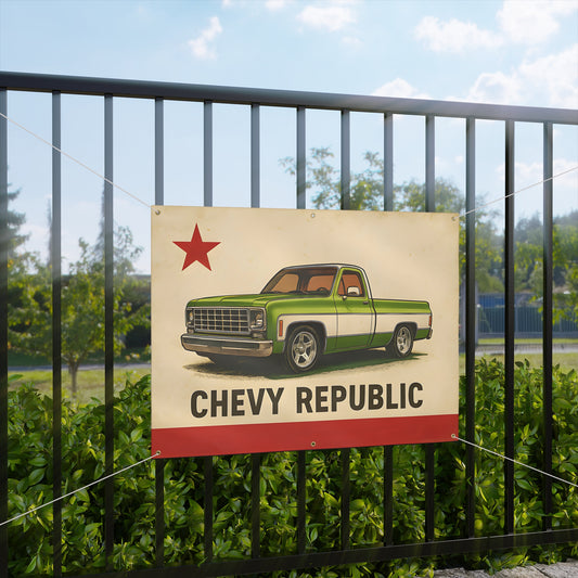 The banner hung on a black metal fence outdoors with green foliage and trees behind it.