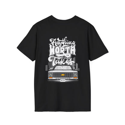 Back of the black t-shirt with a large print reading Anything Worth Having Takes Time in script and block lettering above a squarebody pickup front end with its headlights lit.