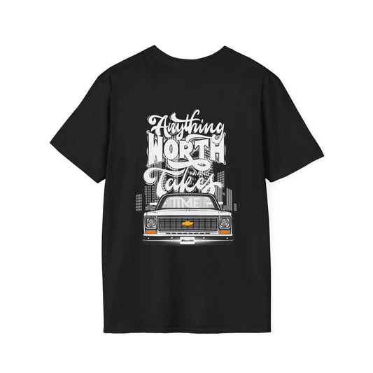 Back of the black t-shirt with a large print reading Anything Worth Having Takes Time in script and block lettering above a squarebody pickup front end with its headlights lit.