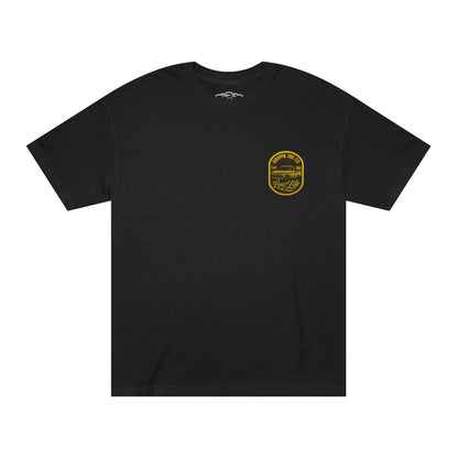 Black t-shirt, front view, with a small left chest print of a gold Drippn Ink Co badge showing a lowered classic pickup truck.